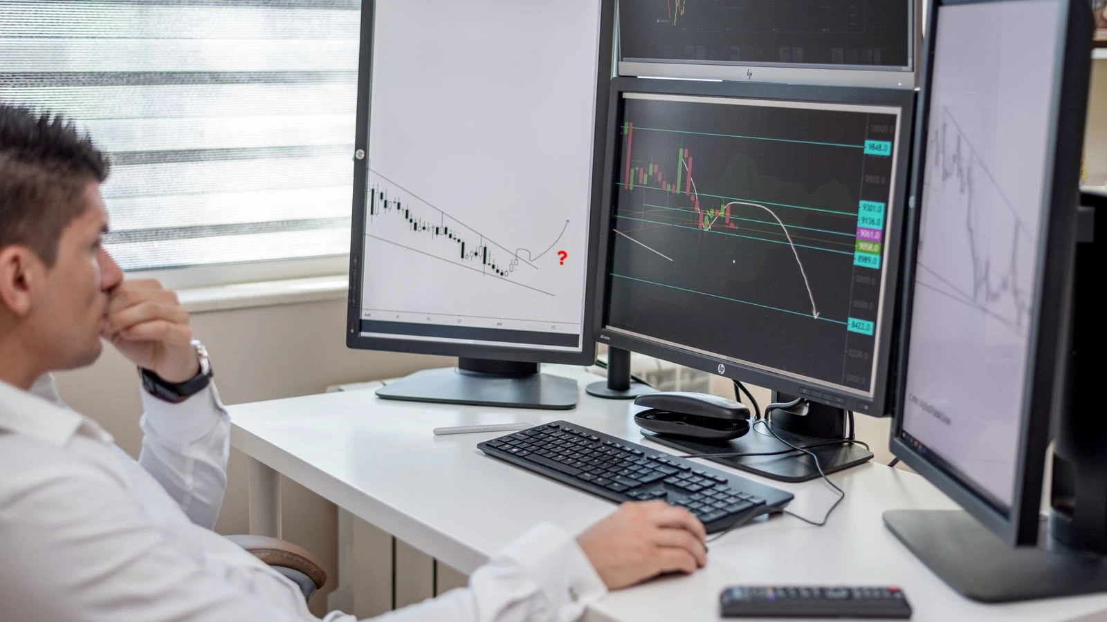 Business professional analyzing financial data on multiple computer monitors at his workspace